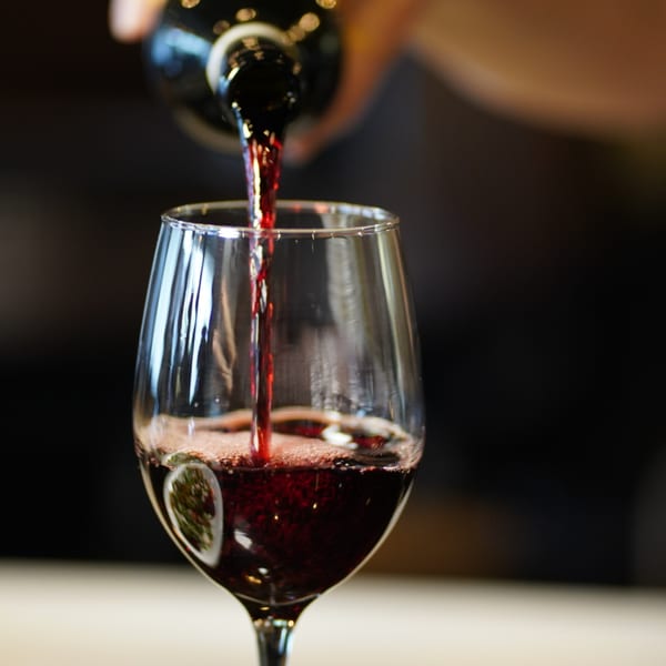 Red wine being poured from a bottle into a clear wine glass, creating bubbles.