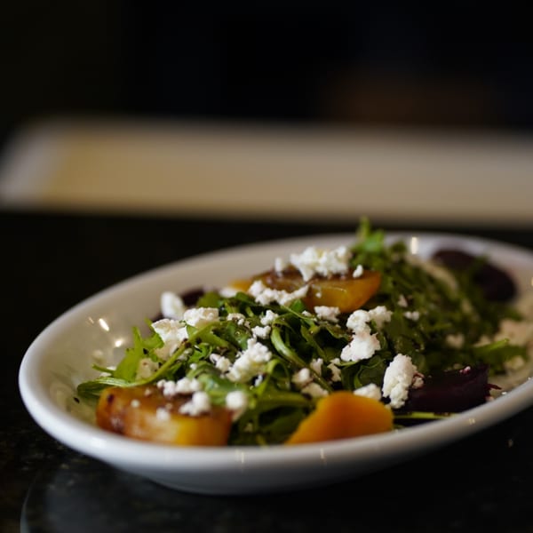 A white bowl filled with a fresh salad of arugula, golden beets, and crumbled feta cheese.