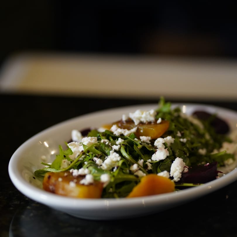 A white bowl filled with a fresh salad of arugula, golden beets, and crumbled feta cheese.